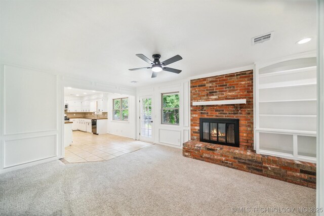 unfurnished living room featuring ceiling fan, light colored carpet, a fireplace, light tile patterned floors, and visible vents