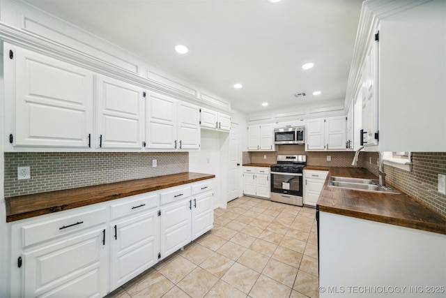 kitchen with decorative backsplash, a sink, white cabinets, wood counters, and stainless steel appliances