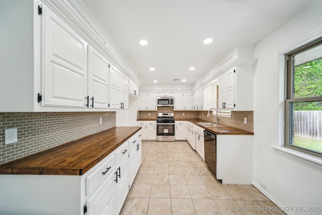 kitchen with appliances with stainless steel finishes, a sink, wooden counters, light tile patterned floors, and tasteful backsplash