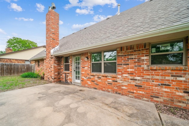 rear view of property with fence, a shingled roof, a chimney, and brick siding