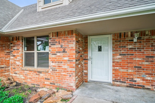 property entrance with a shingled roof and brick siding