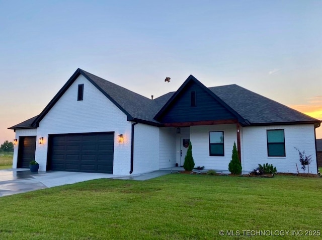 view of front of house with brick siding, a shingled roof, a yard, and concrete driveway