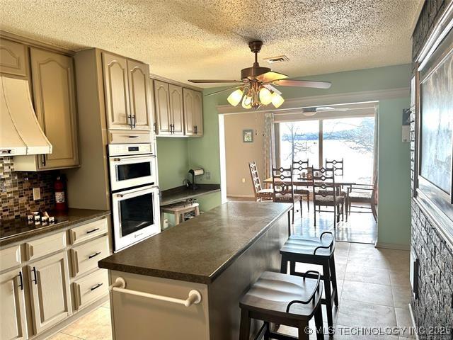 1082 Gaines Creek Loop, Eufaula, OK 74432 - kitchen with premium range hood, dark countertops, black electric stovetop, white double oven, and ceiling fan