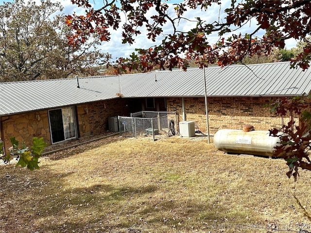 back of property with central AC unit, fence, stone siding, and metal roof