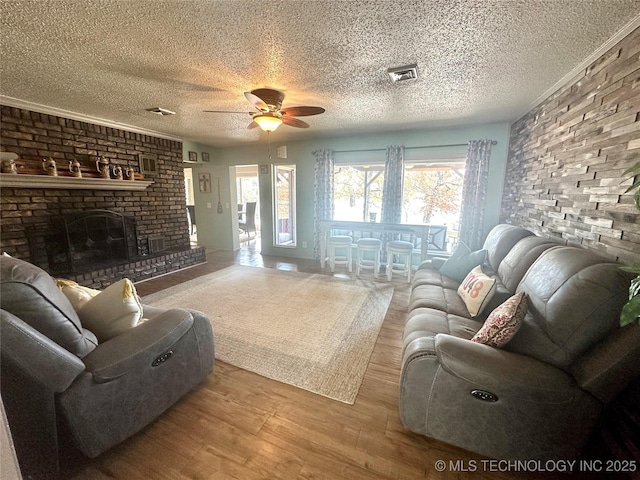 living room with a brick fireplace, a textured ceiling, ceiling fan, and wood finished floors