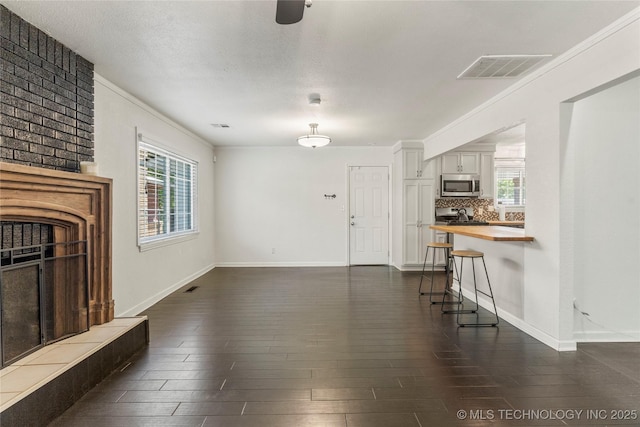 unfurnished living room with a large fireplace, plenty of natural light, dark wood-style flooring, and visible vents