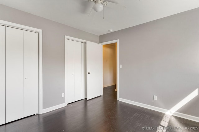 unfurnished bedroom with multiple closets, baseboards, a ceiling fan, and wood finished floors