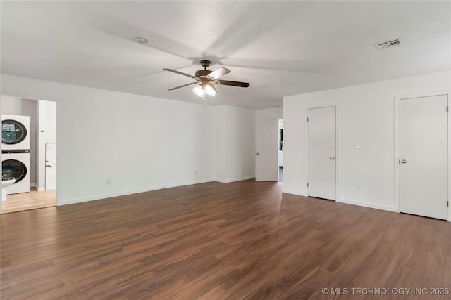 unfurnished living room with ceiling fan, baseboards, visible vents, dark wood-style floors, and stacked washer and clothes dryer