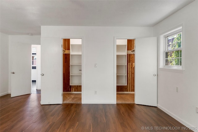 unfurnished bedroom with baseboards, wood finished floors, and a spacious closet