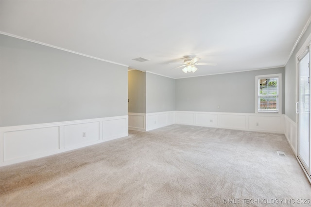 carpeted empty room with a ceiling fan, a decorative wall, a wainscoted wall, and ornamental molding