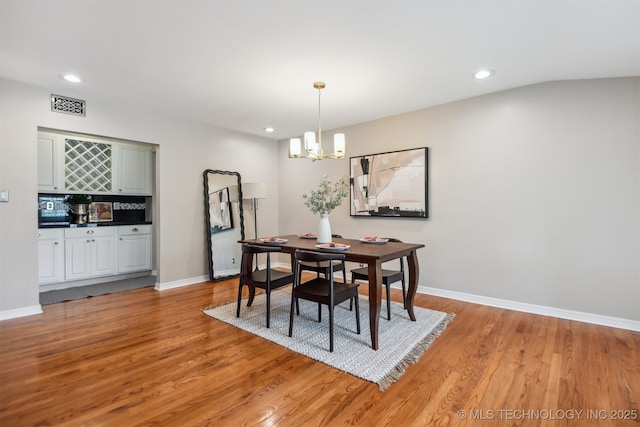 dining room featuring visible vents, light wood finished floors, an inviting chandelier, and indoor bar