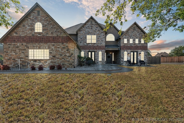 traditional home with a lawn, a patio, fence, and stone siding