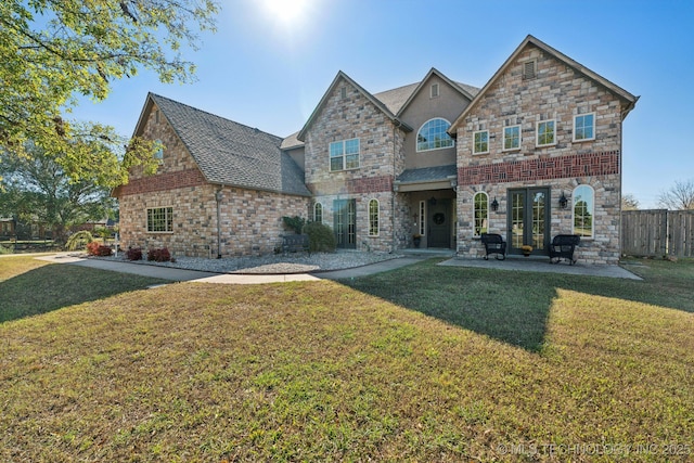 view of front facade with fence, stone siding, a front yard, roof with shingles, and a patio area