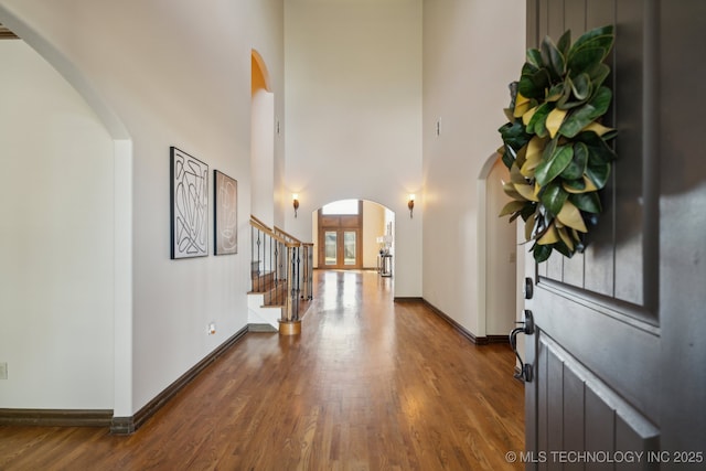 foyer entrance featuring stairway, arched walkways, dark wood finished floors, and a towering ceiling