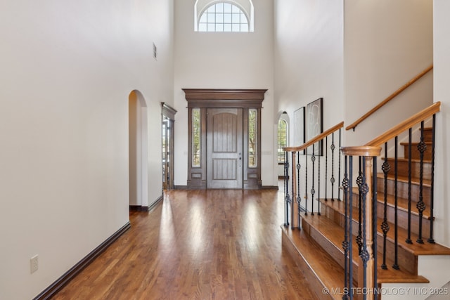 entrance foyer with a towering ceiling, arched walkways, wood finished floors, stairway, and baseboards