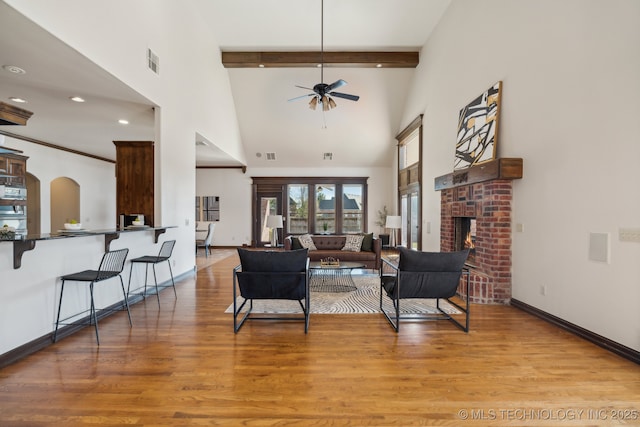living room featuring ceiling fan, high vaulted ceiling, wood finished floors, beamed ceiling, and visible vents