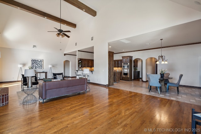 living room with arched walkways, ceiling fan with notable chandelier, high vaulted ceiling, and wood finished floors