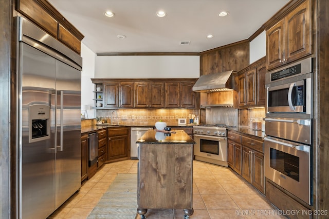 kitchen with a kitchen island, high end appliances, light tile patterned floors, and wall chimney exhaust hood