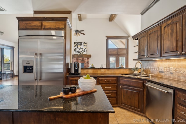 kitchen featuring vaulted ceiling with beams, a sink, dark stone countertops, backsplash, and stainless steel appliances