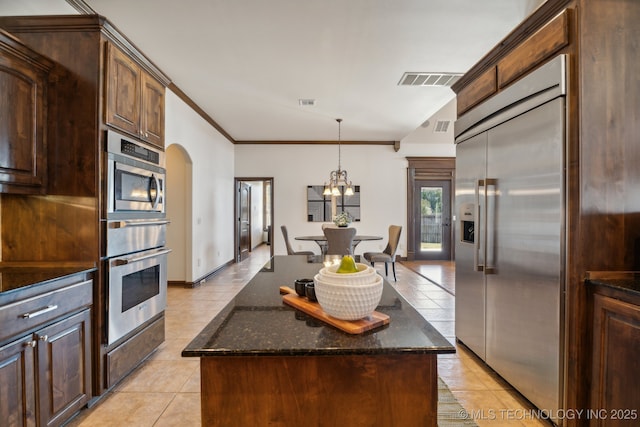 kitchen featuring light tile patterned floors, built in appliances, dark stone counters, and visible vents