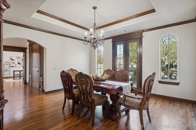 dining area with arched walkways, wood finished floors, baseboards, a raised ceiling, and a chandelier