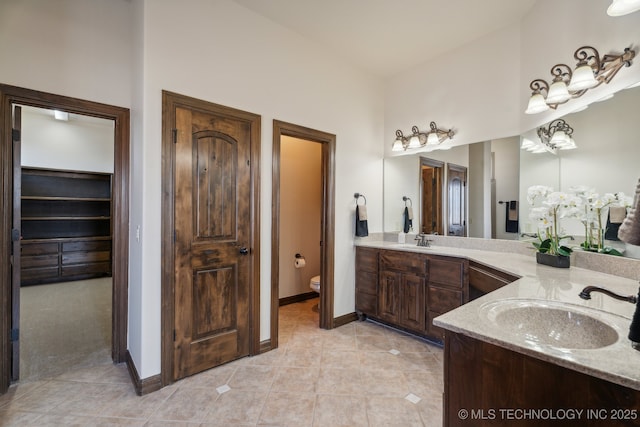full bath with baseboards, a sink, double vanity, and toilet