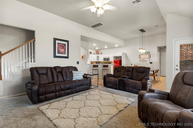 living room with stairway, visible vents, ceiling fan, and light colored carpet