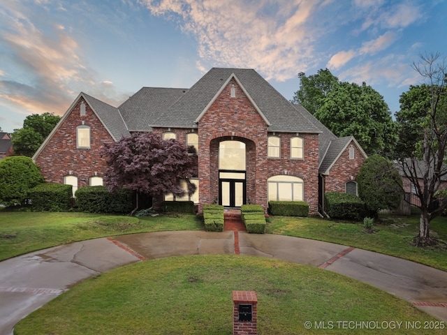 traditional-style house with brick siding, a front lawn, and roof with shingles