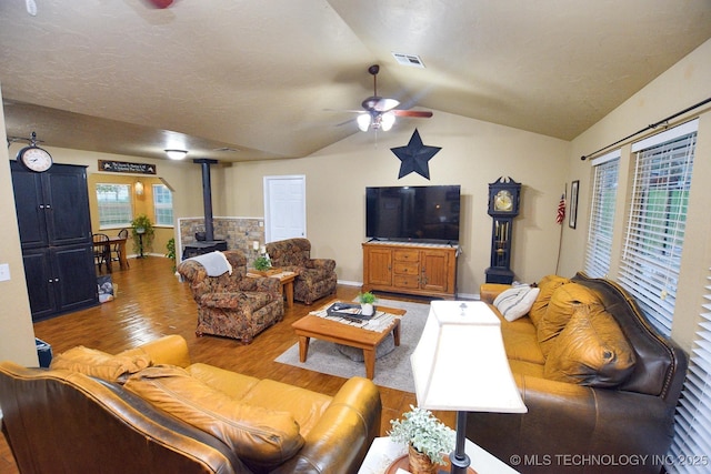 living room with ceiling fan, visible vents, vaulted ceiling, a wood stove, and light wood-style floors