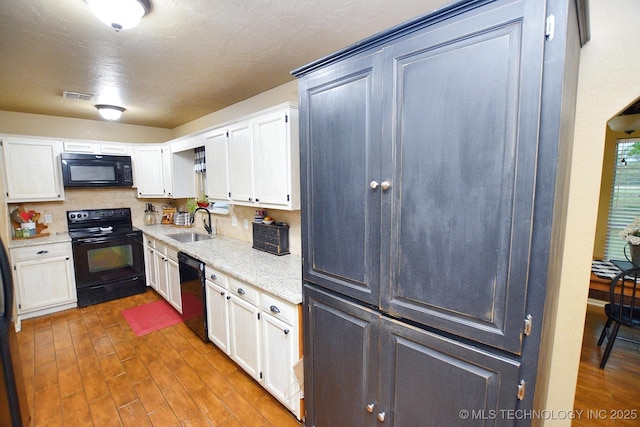 kitchen featuring visible vents, wood finished floors, a sink, black appliances, and white cabinetry
