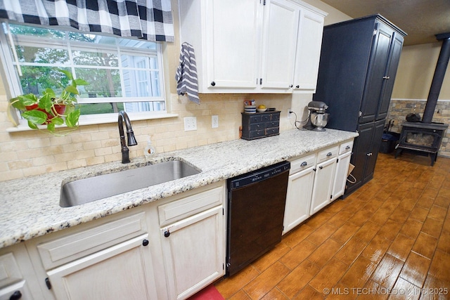 kitchen with decorative backsplash, a wood stove, a sink, black dishwasher, and white cabinetry