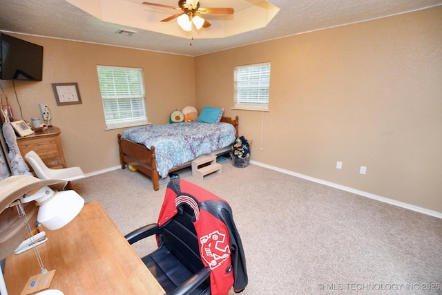 carpeted bedroom featuring baseboards, ceiling fan, a raised ceiling, and visible vents