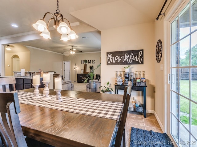 tiled dining room with crown molding, arched walkways, baseboards, and ceiling fan with notable chandelier