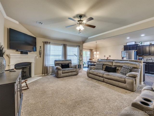 living area featuring visible vents, crown molding, a fireplace with raised hearth, ceiling fan with notable chandelier, and light carpet