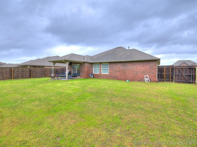 rear view of property with a yard, brick siding, and a fenced backyard