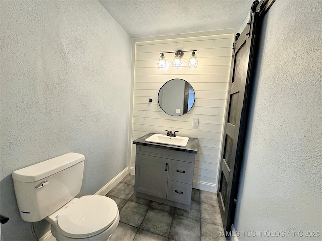 bathroom featuring a textured wall, vanity, toilet, a textured ceiling, and baseboards