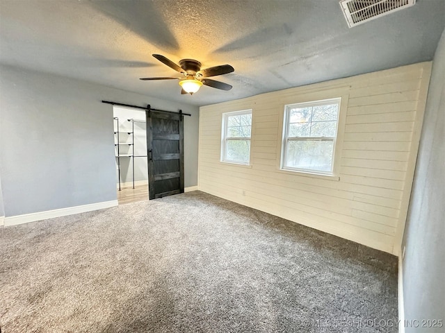 unfurnished room featuring visible vents, a barn door, a textured ceiling, a ceiling fan, and carpet