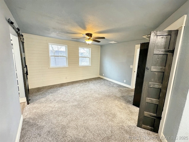 unfurnished bedroom with ceiling fan, a barn door, a textured ceiling, carpet, and baseboards