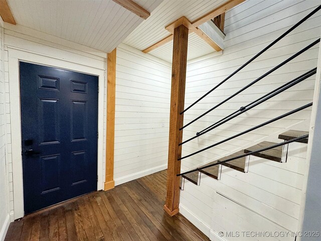 entrance foyer featuring stairway, baseboards, beamed ceiling, wooden walls, and dark wood-type flooring