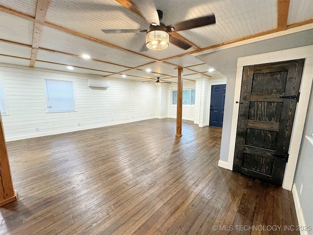 unfurnished living room featuring wooden walls, baseboards, ceiling fan, and dark wood-style floors
