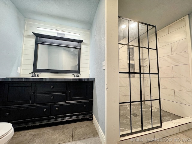 bathroom featuring a walk in shower, a textured wall, double vanity, toilet, and baseboards