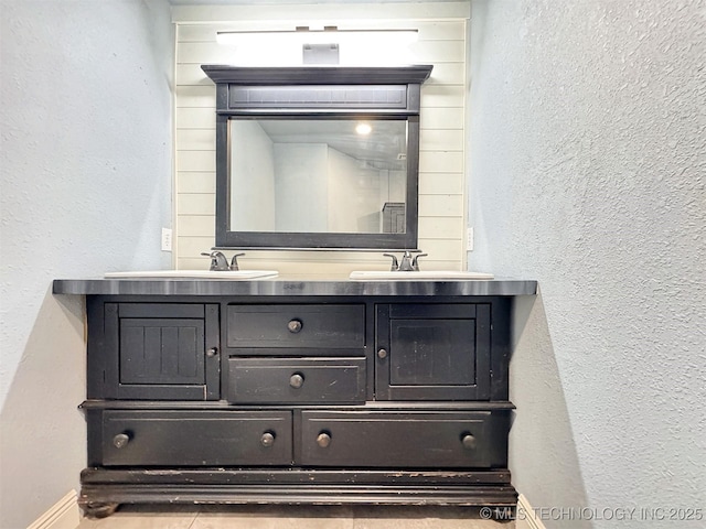 bathroom featuring baseboards, a sink, a textured wall, and double vanity