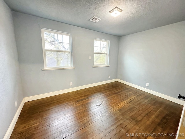 spare room featuring a textured ceiling, visible vents, a healthy amount of sunlight, and dark wood-type flooring