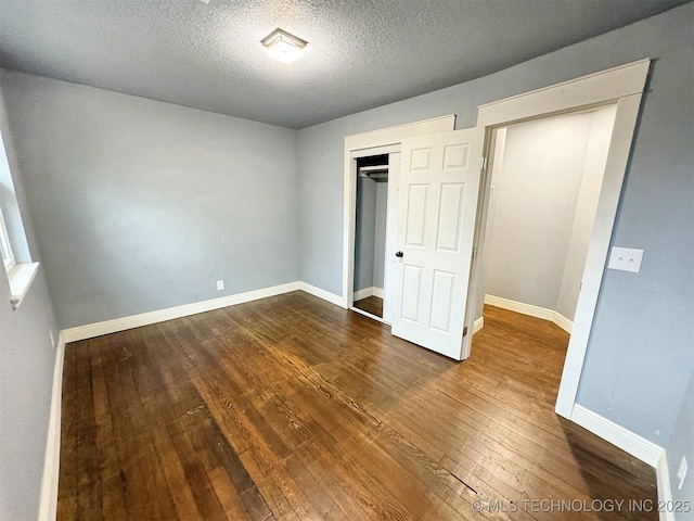 unfurnished bedroom featuring baseboards, a closet, dark wood-style floors, and a textured ceiling