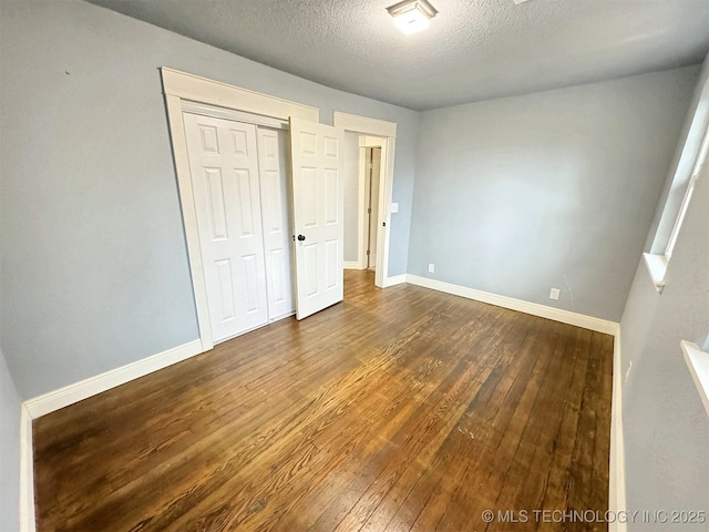 unfurnished bedroom featuring baseboards, a closet, dark wood-style floors, and a textured ceiling