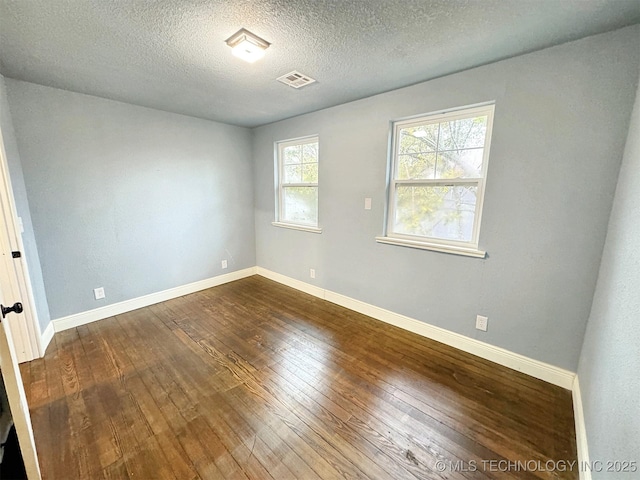 empty room with baseboards, a textured ceiling, visible vents, and dark wood finished floors
