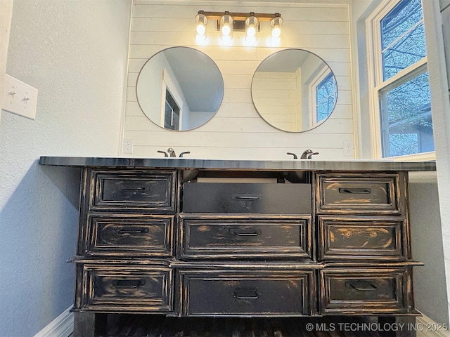 bathroom with baseboards, double vanity, and a textured wall