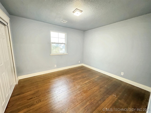 spare room featuring a textured ceiling, visible vents, dark wood-style floors, and baseboards