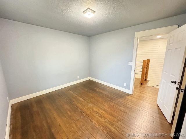 spare room with a textured ceiling, dark wood-style floors, and baseboards