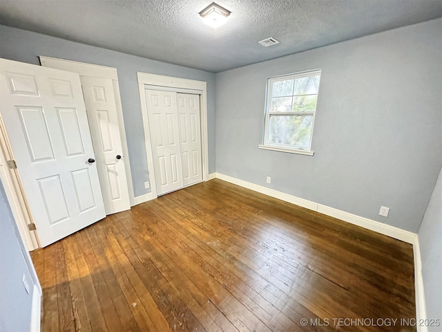 unfurnished bedroom with visible vents, a textured ceiling, dark wood-style flooring, and baseboards